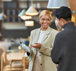 Smiling woman in a retail store shows a customer what's on her tablet device
