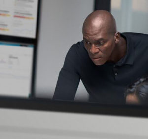 Man looking over the shoulder of someone who is working on a desktop computer