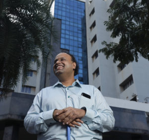 A man who is blind holds his guide cane as he stands in front of an office building