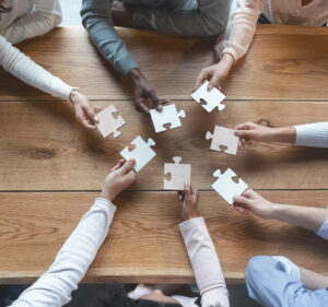 Seven hands holding puzzle pieces over a table