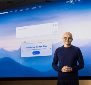 Man smiles as he stands in front of a large screen introducing the new Bing