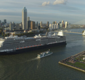 The cruise ship Rotterdam departs an urban port during daylight hours.