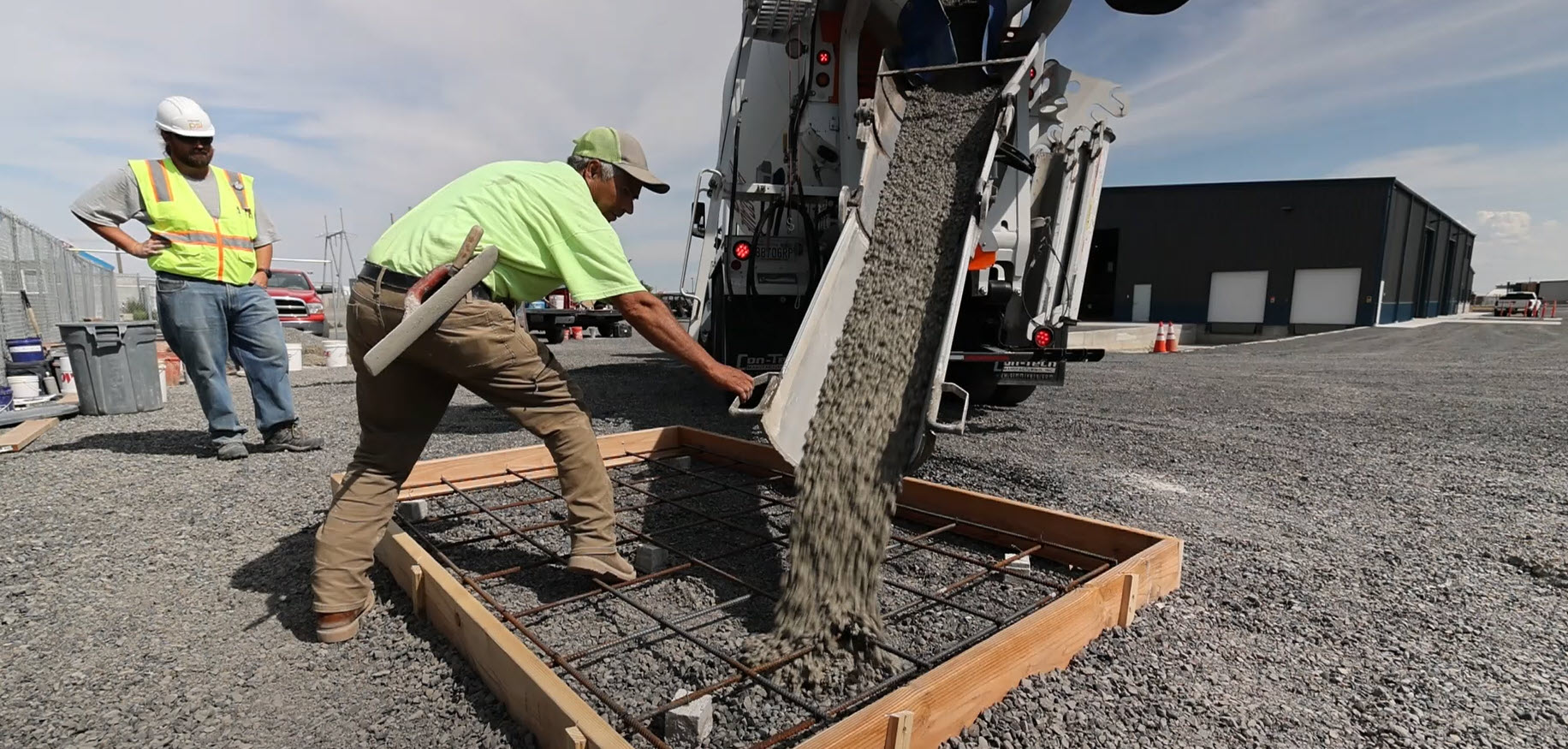 Construction worker pours concrete into a table-top size wooden frame.