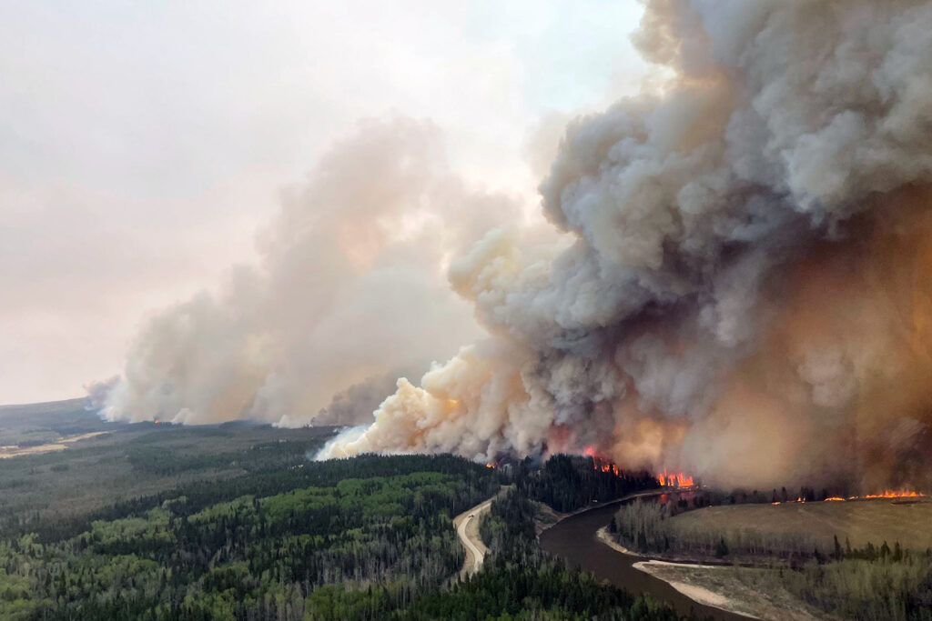 A large fire by a river with heavy smoke billowing into the sky