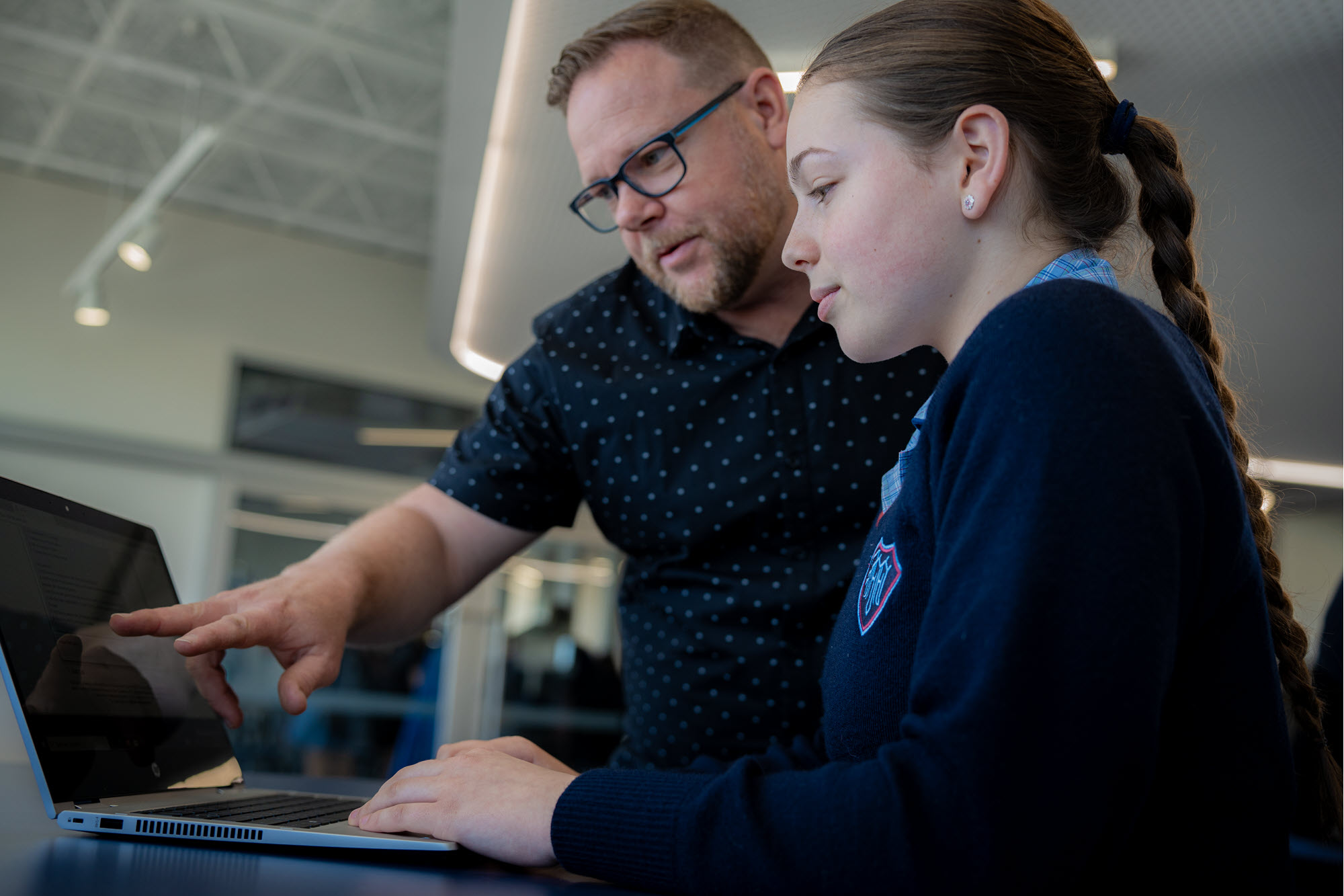 A teacher helping a student who is working with EdChat on a computer.
