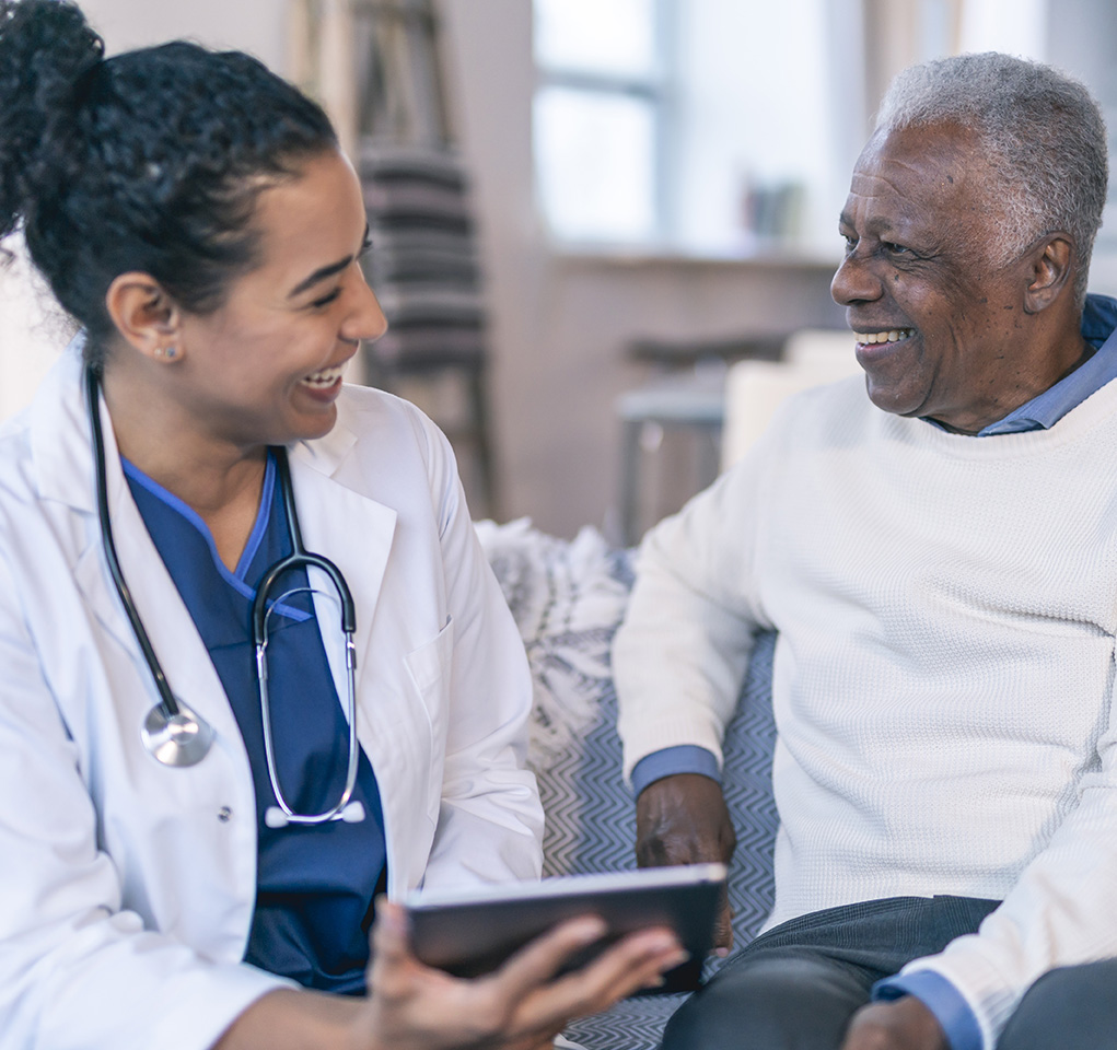 Female doctor and senior male patient share a smile as she holds a tablet device