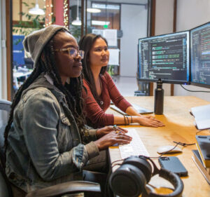 Two women viewing monitors of a desktop computer