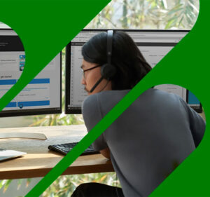 Man wearing a headset and working on a laptop computer attached to two monitors