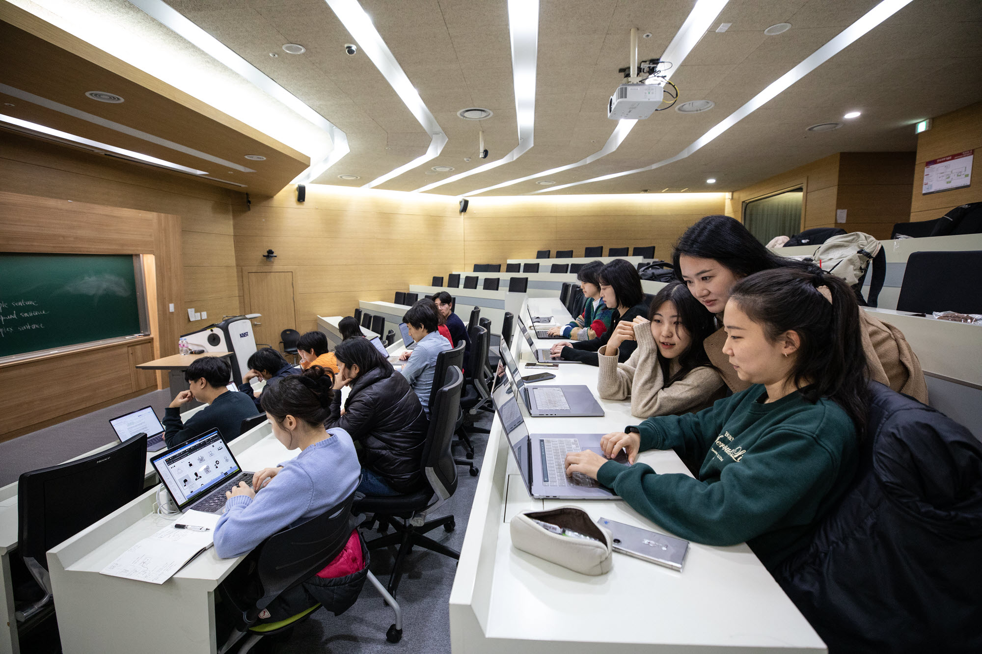 Photo of female professor talking with two female students seated with computers in a lecture hall at the Korea Advanced Institute of Science and Technology.