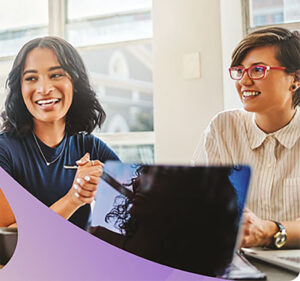 Two women in an office smiling and looking at someone off-camera