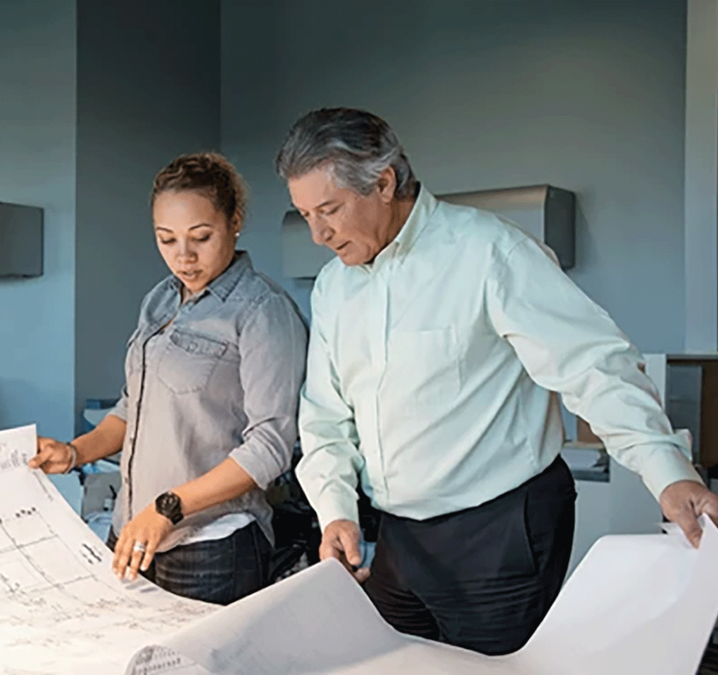 Two people reviewing large architectural charts in an office building