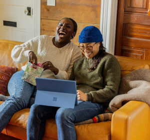 Two people sitting on a couch enjoying what they're watching on their Microsoft Surface device