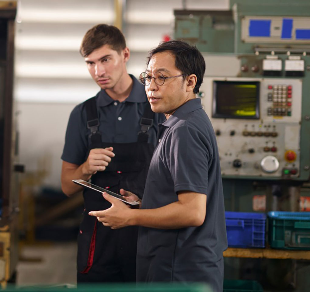 Two men in an industrial setting looking at data on screens
