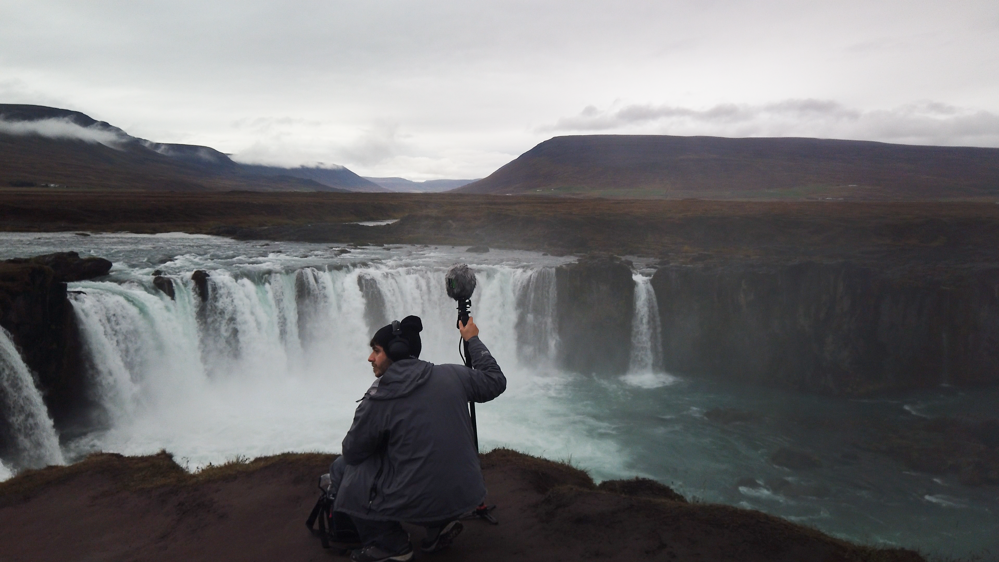 Man holding a microphone across from a waterfall