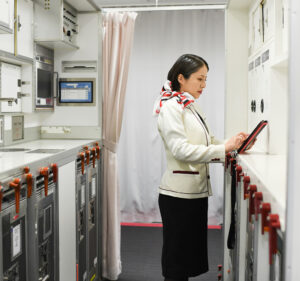 A woman in a flight attendant’s uniform taps on a tablet in an airplane galley.