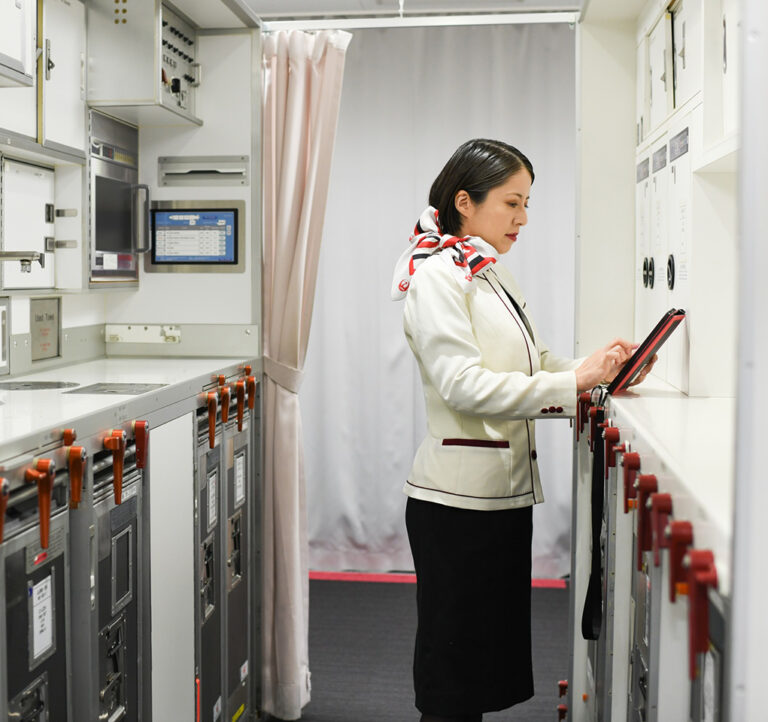 A woman in a flight attendant’s uniform taps on a tablet in an airplane galley.
