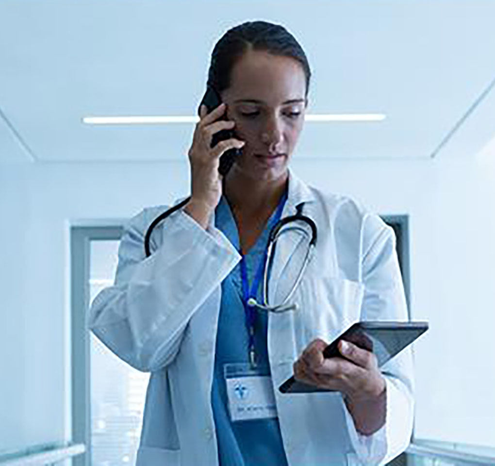Healthcare professional talking on her phone as she looks at her tablet device