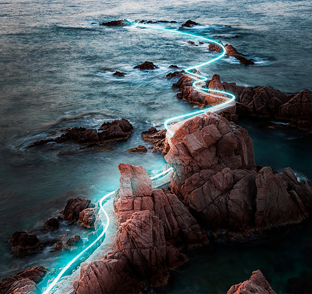 A line of light winding its way through rocks along a coast.