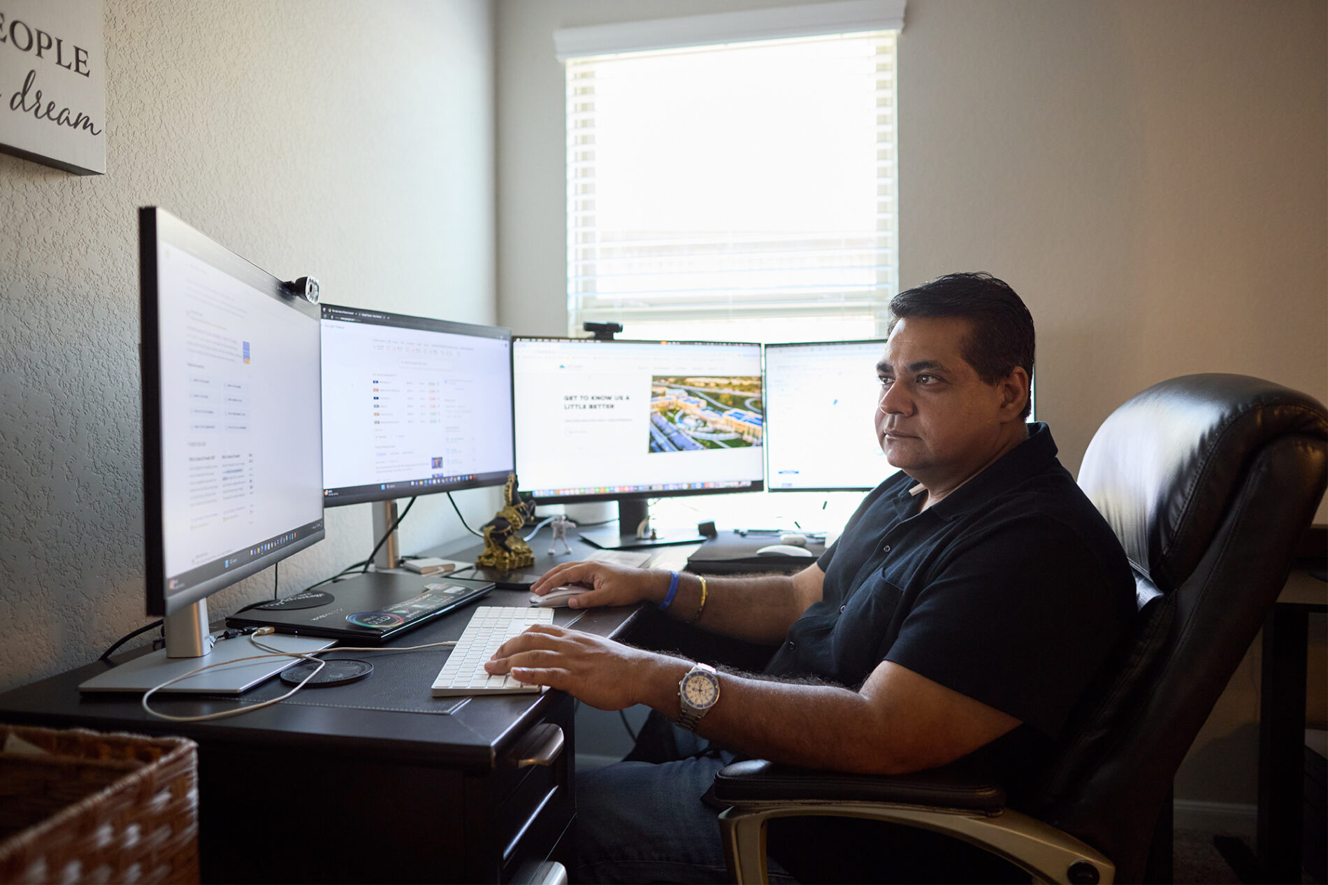 A man in a black shirt types on a keyboard at a desk crowded with four computer screens.
