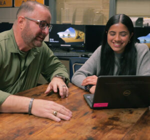 Teacher and teen student interacting as they view a laptop computer.