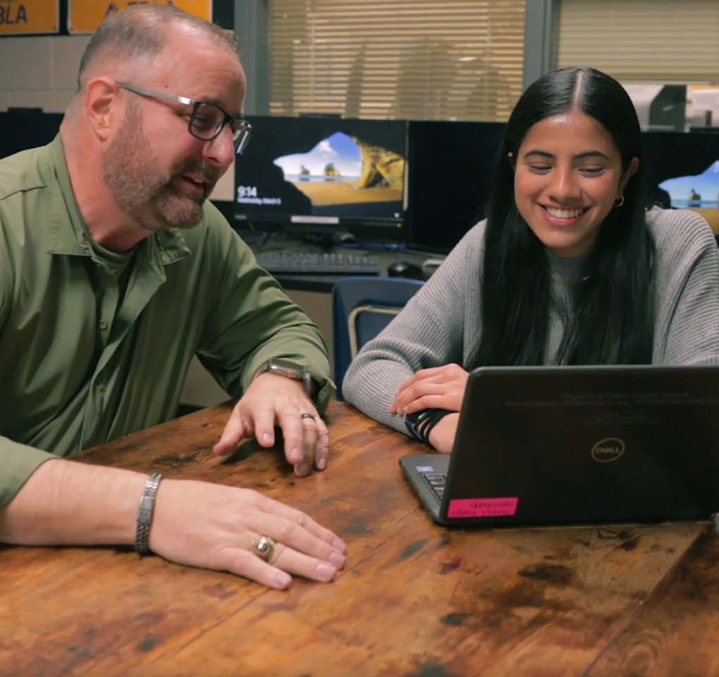 Teacher and teen student interacting as they view a laptop computer.