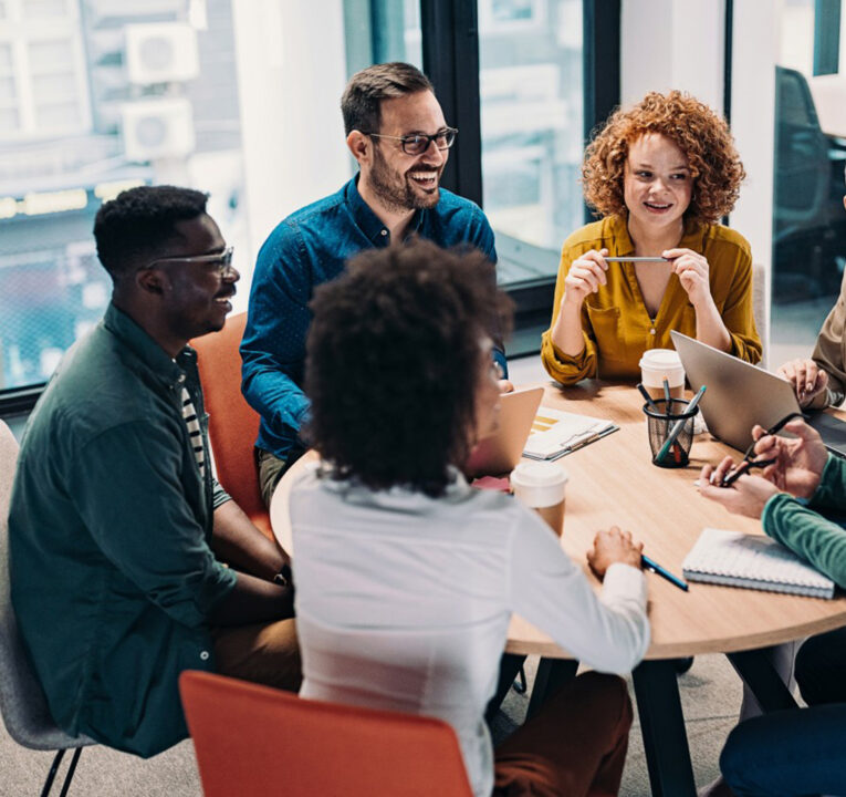 People smiling as they sit around a table for a work meeting.