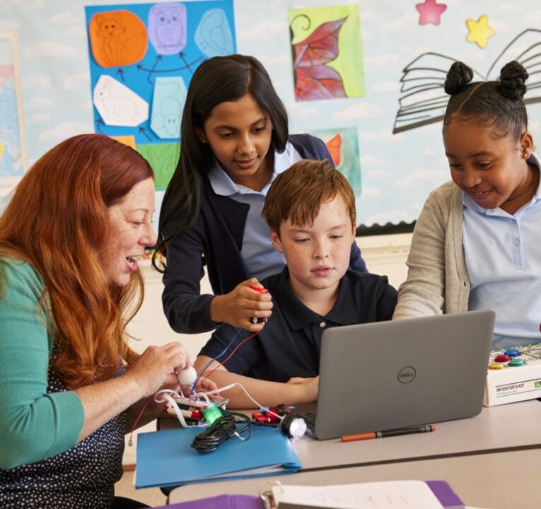 A teacher and three students gather around a laptop computer