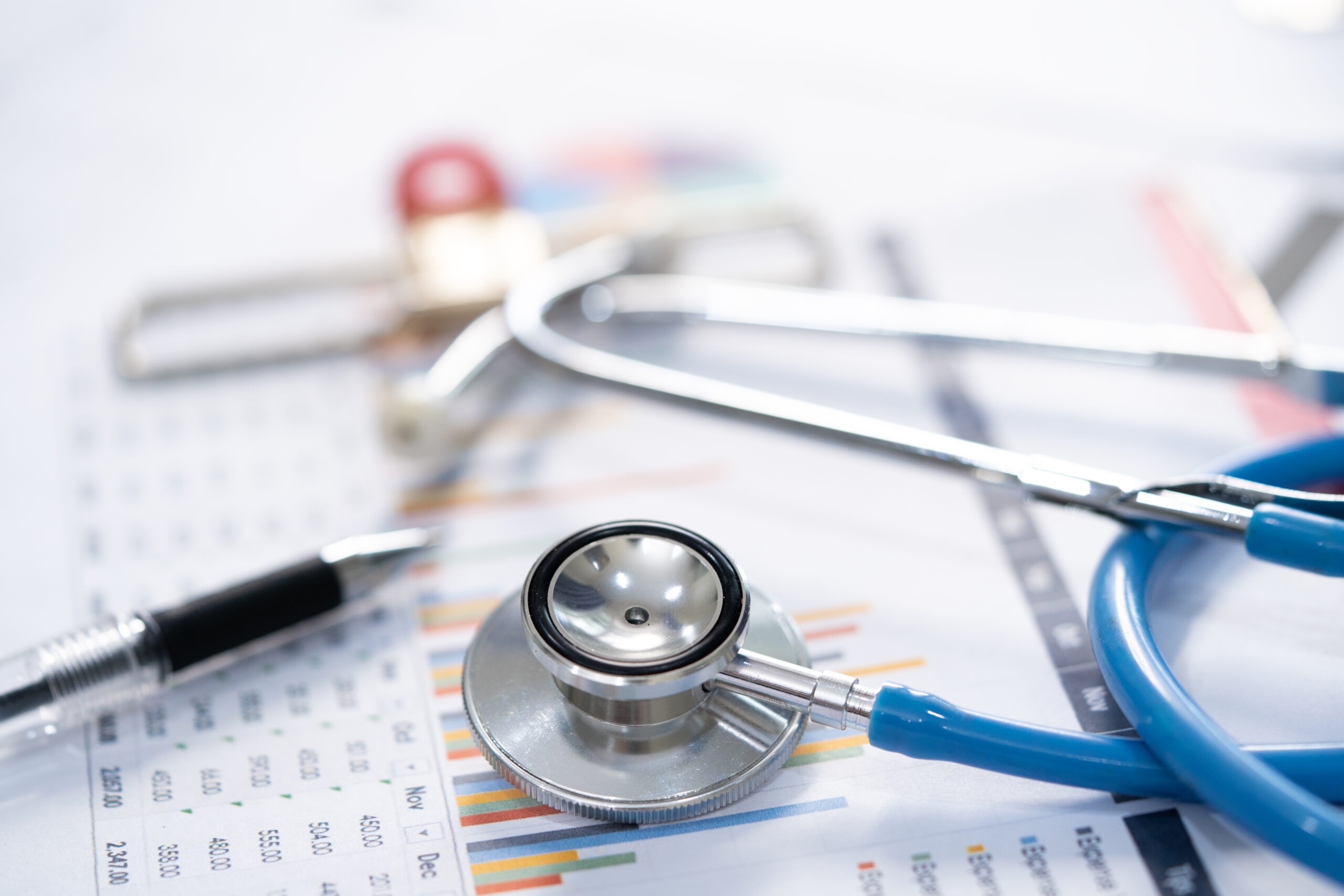 A stethoscope and pen rest on top of medical charts and data sheets.