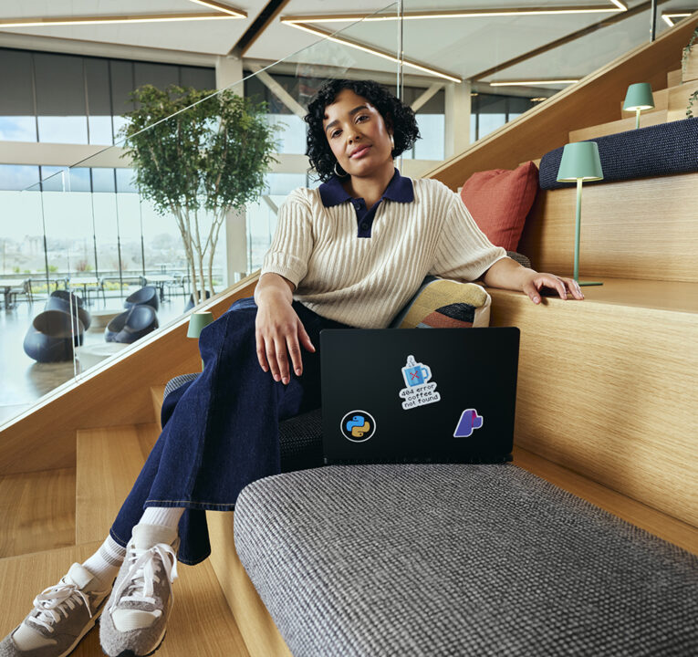 Woman with a laptop sitting on wooden steps in an open space.