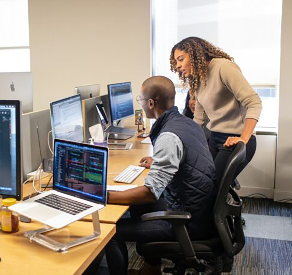 Two people in an office discussing what's on the monitor before them.