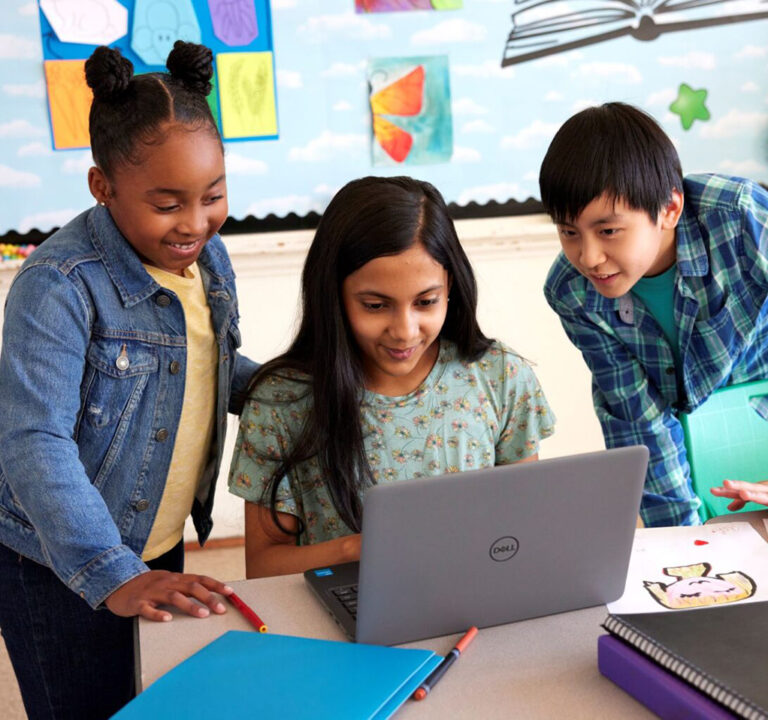 Three kids sharing a laptop computer in a classroom.