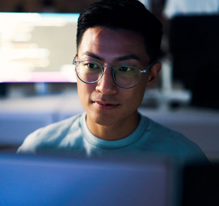 A man wearing glasses looks at his computer screen.