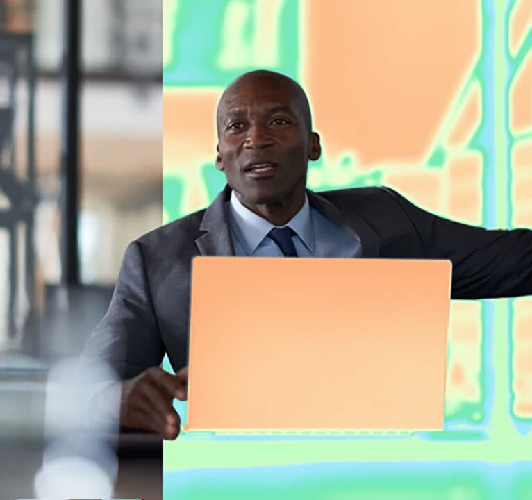 Man wearing a suit and tie talks as he interacts with a laptop computer.