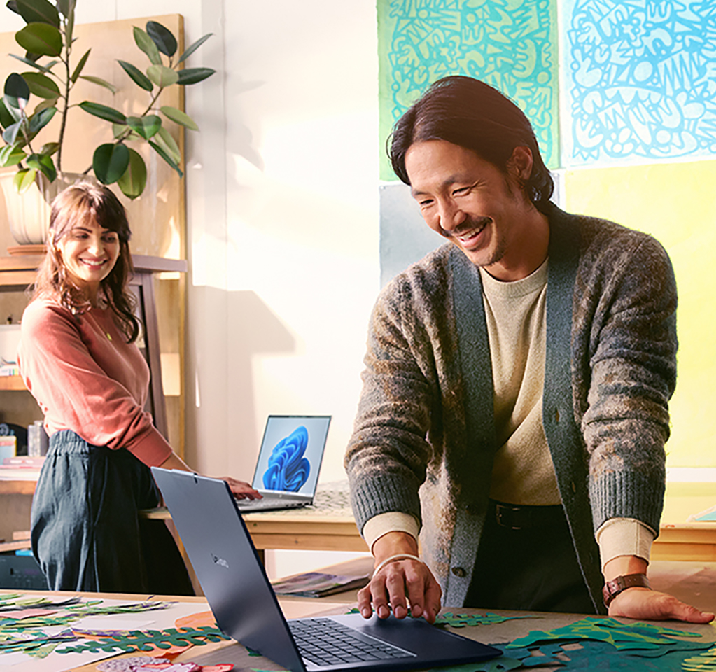 Three people smiling as they work on laptop computers in a creative studio.