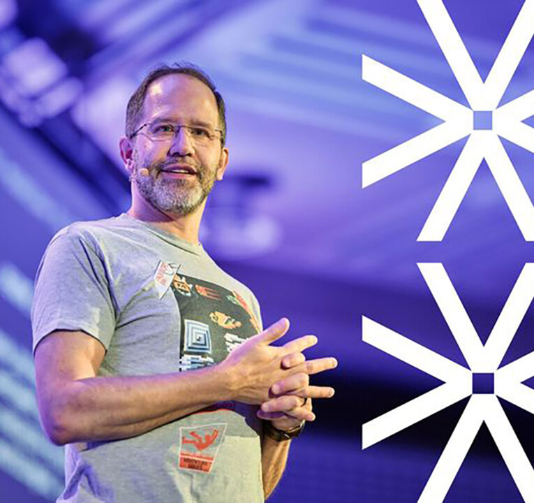 Man on a stage clasping his hands together.